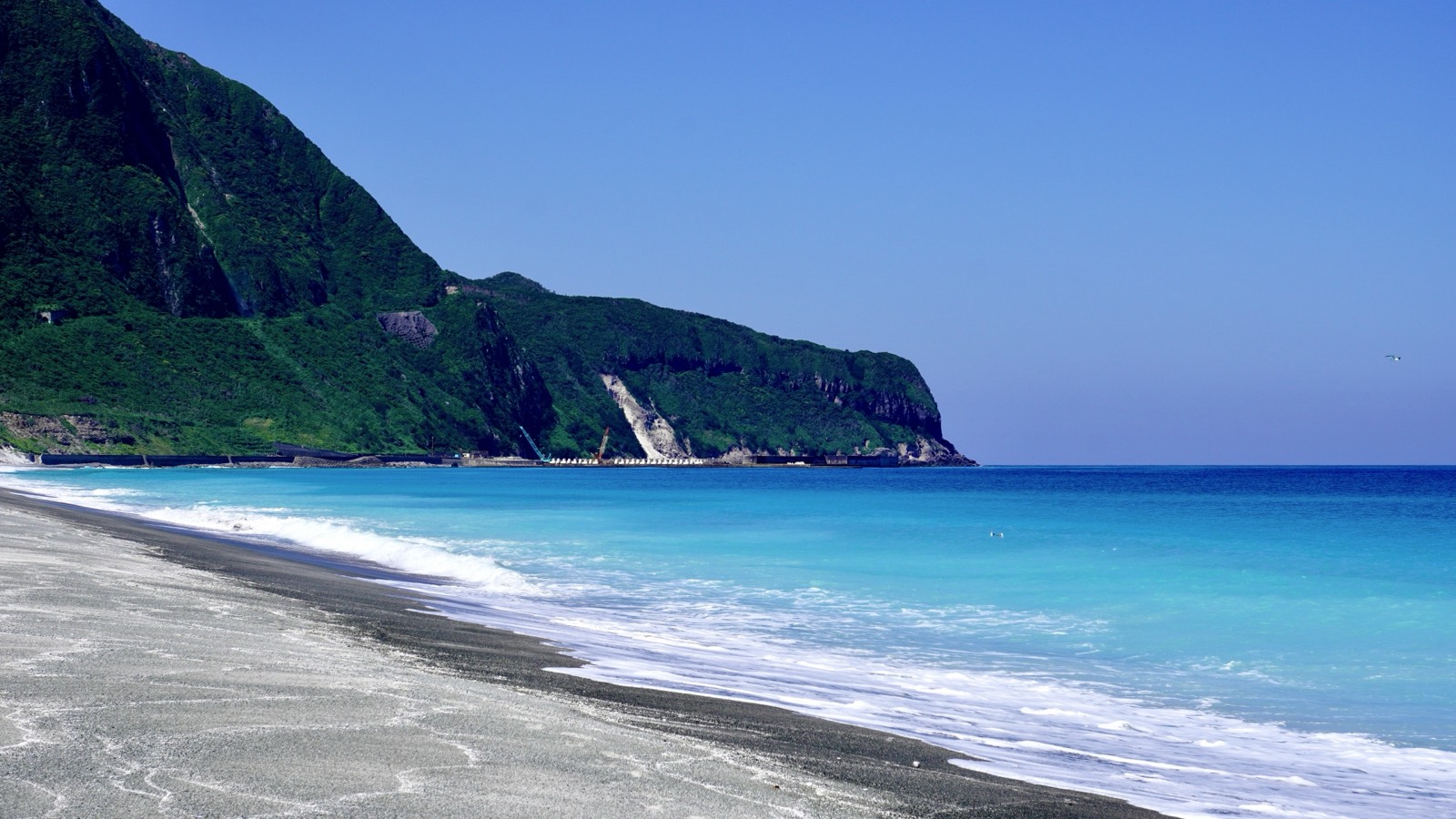 新島の海。黒い砂浜と青いグラデーションの海、緑の断崖